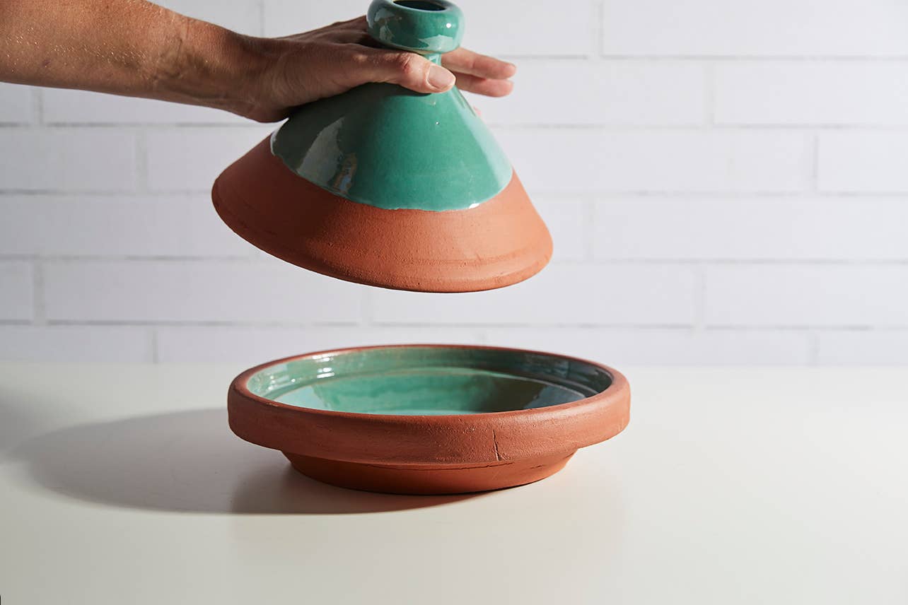 Terracotta tagine with white top on a light surface with a white tiled wall background