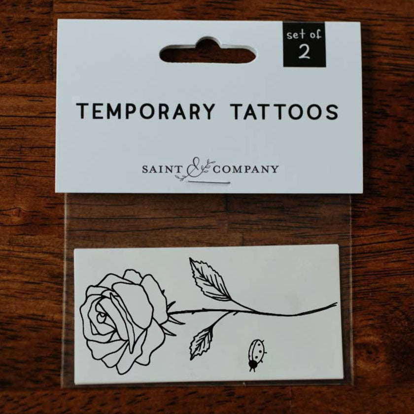 Person wearing a white long-sleeve shirt and blue jeans with a small rose tattoo on their arm.