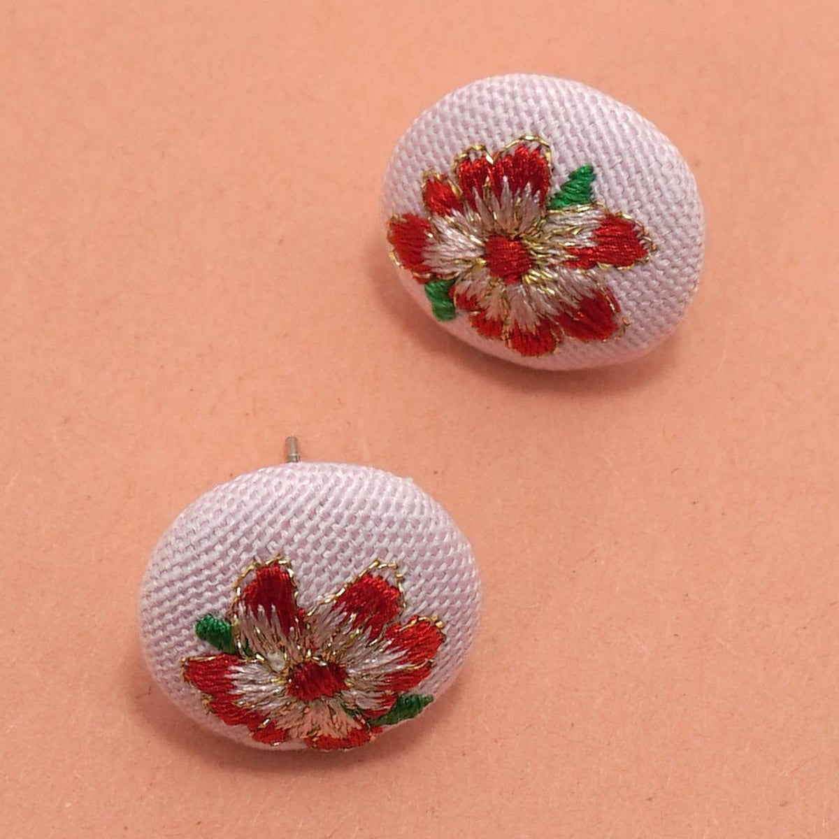 Pair of white earrings with red and green floral designs on a peach background