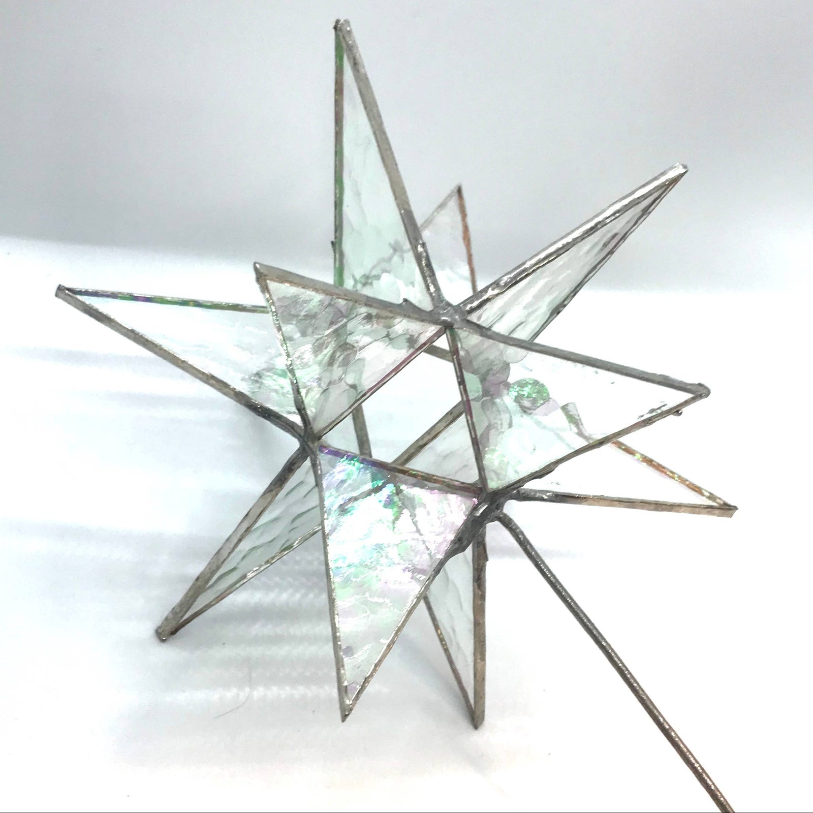 A geometric star-shaped stained glass ornament with iridescent green and blue patterned glass panels and dark metal frames, photographed on a white background.