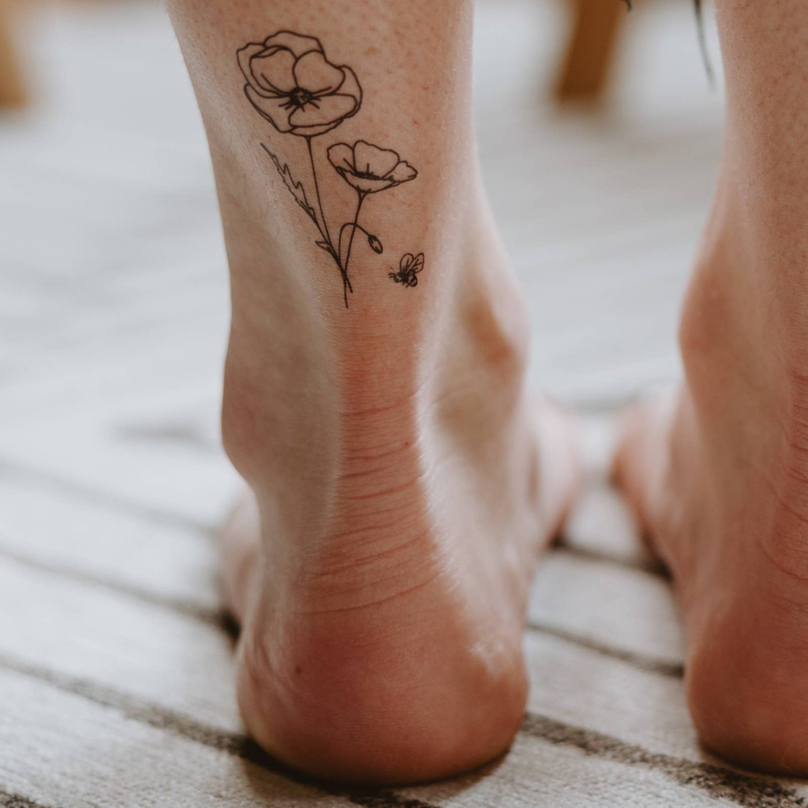 Close-up of feet with floral tattoos on a textured floor.
