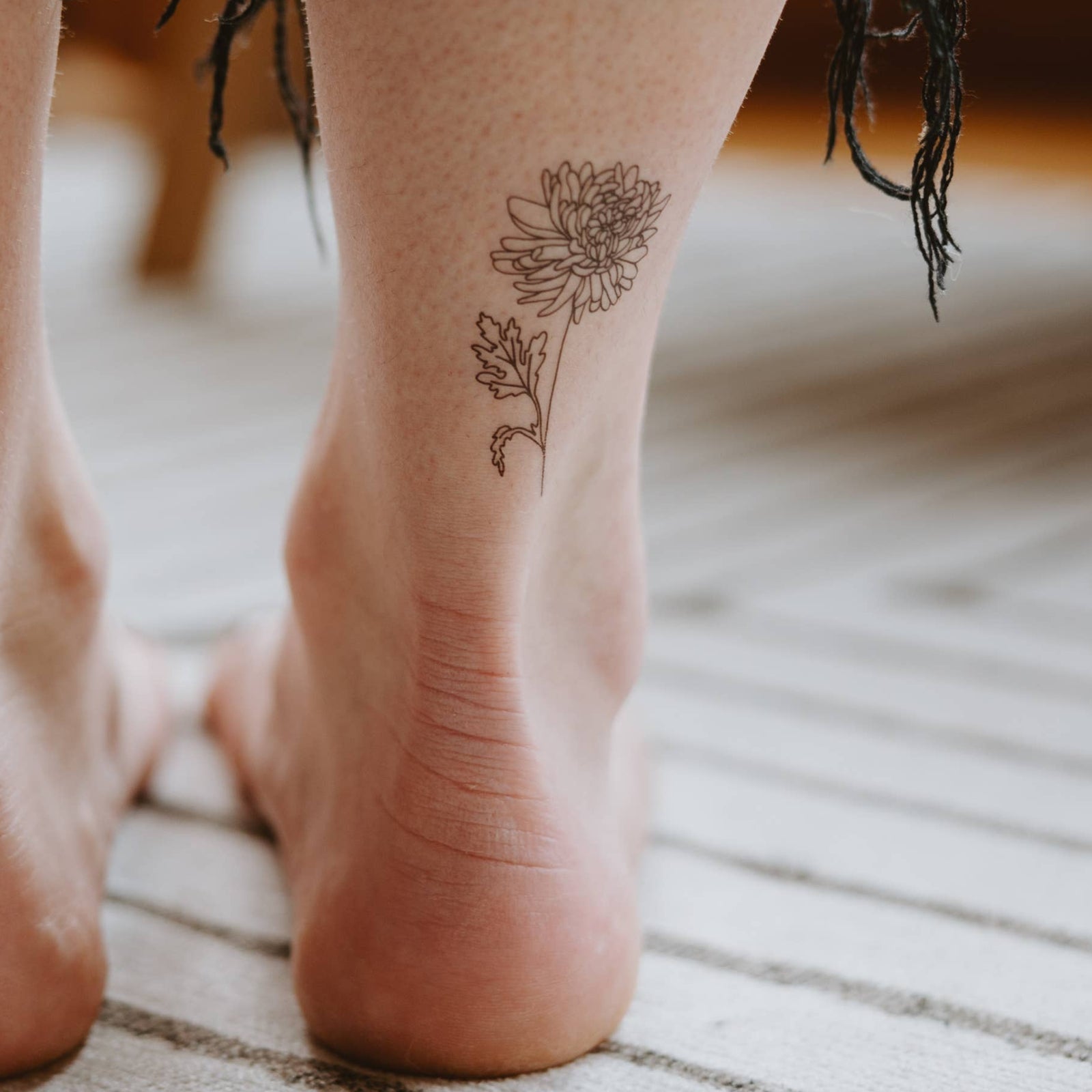 Close-up of feet with floral tattoos on a textured floor.