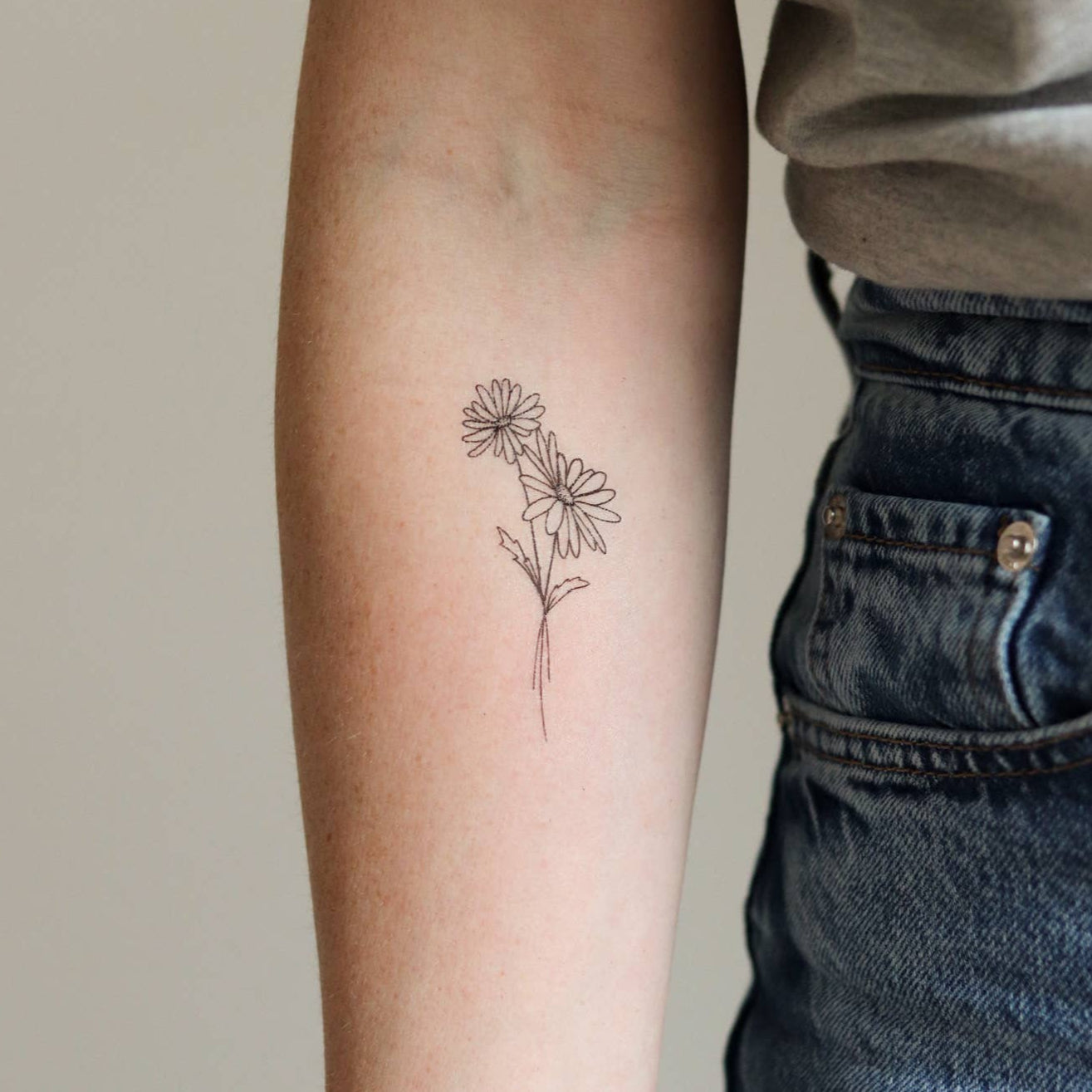 Person wearing a small floral tattoo on their arm against a neutral background