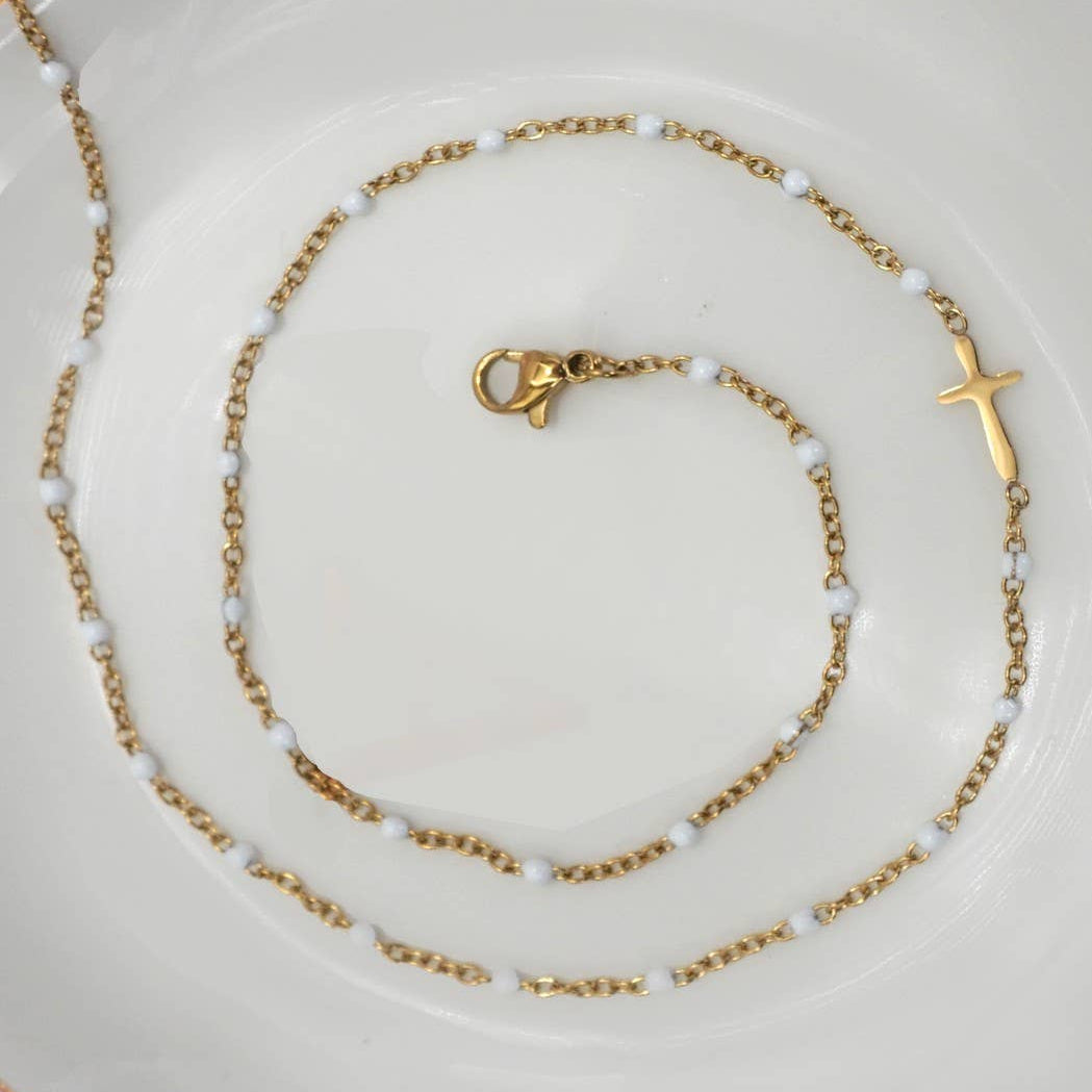 Gold necklace with a cross pendant on a white plate with a pink background