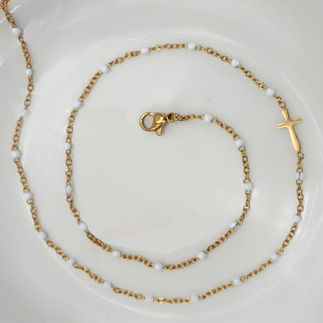 Gold necklace with a cross pendant on a white plate with a pink background