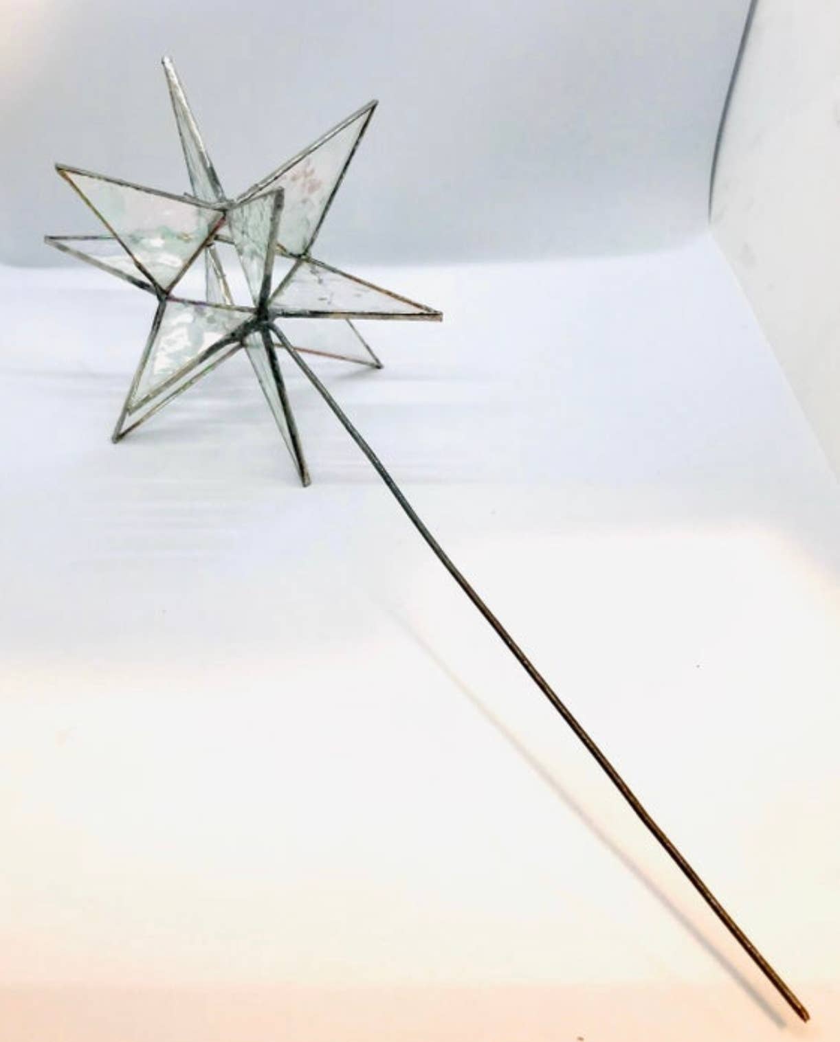 A geometric star-shaped stained glass ornament with iridescent green and blue patterned glass panels and dark metal frames, photographed on a white background.