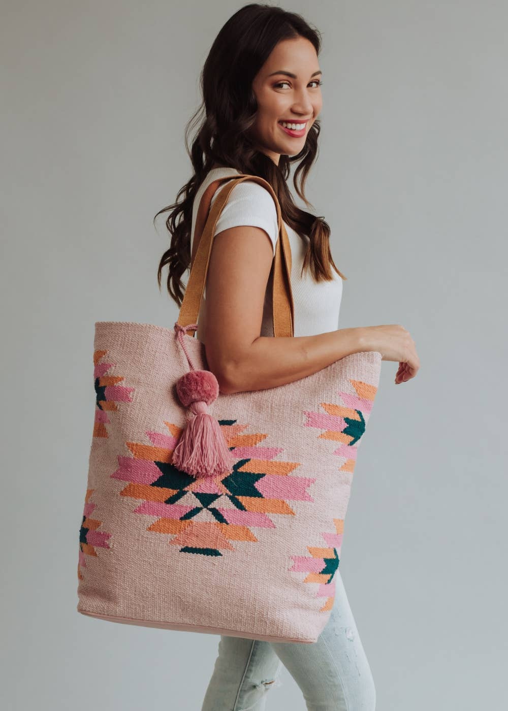 Tote bag with geometric pattern and pink tassel held by a person wearing jeans.