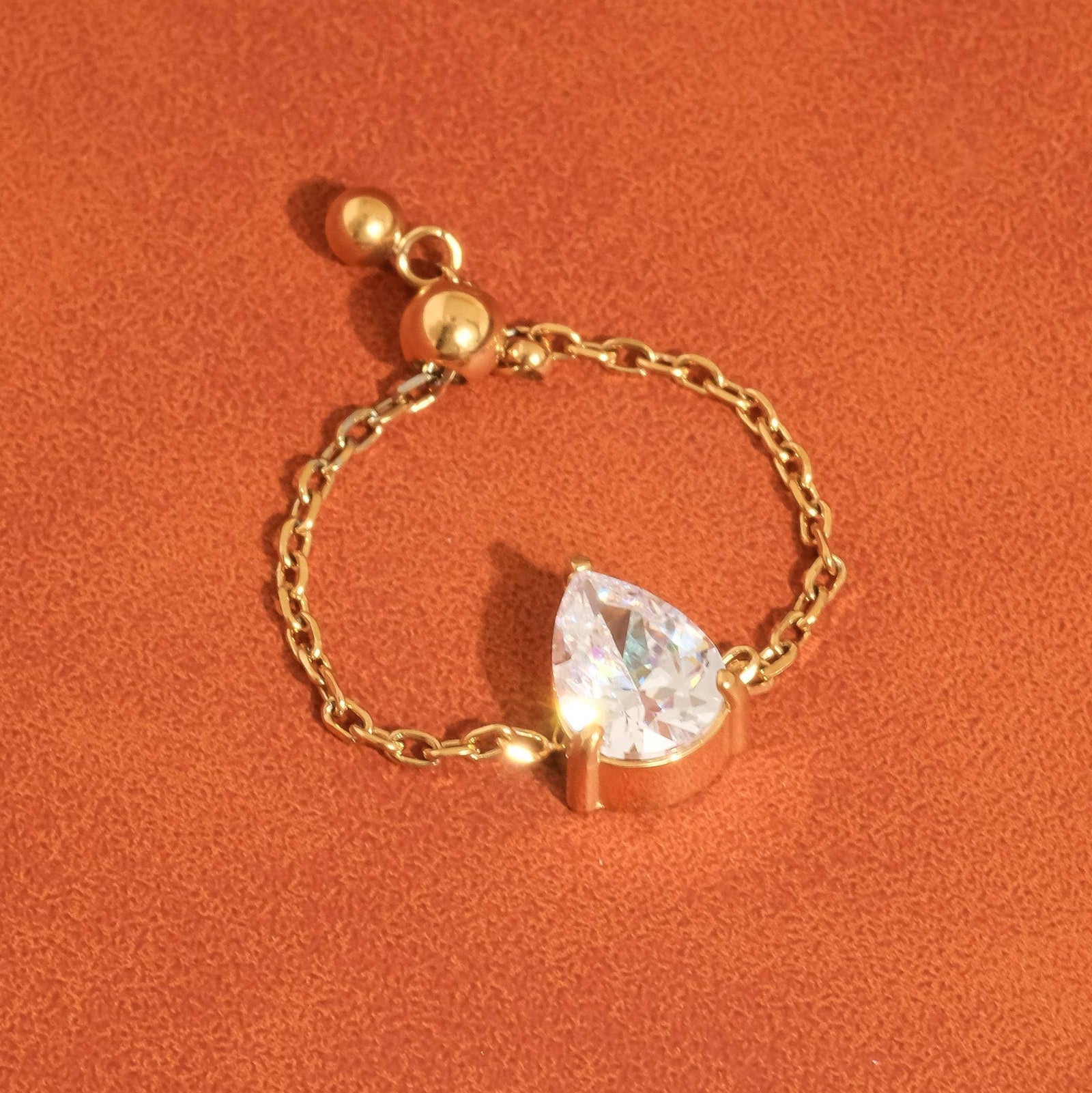 Gold bracelet with a teardrop-shaped crystal on an orange background
