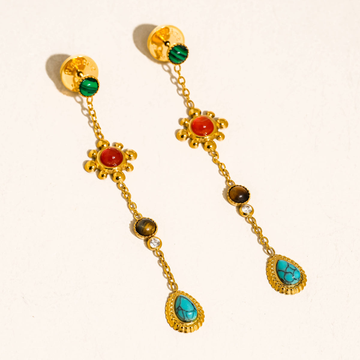 Gold earrings with colorful gemstones on a beige background