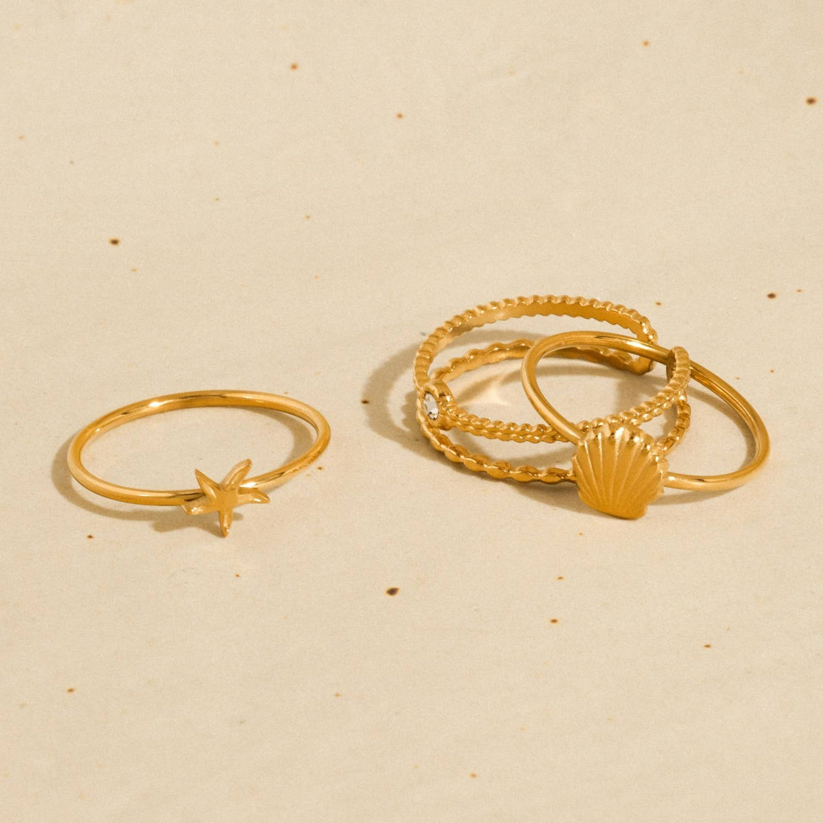 Two gold rings with star and shell designs on a beige background