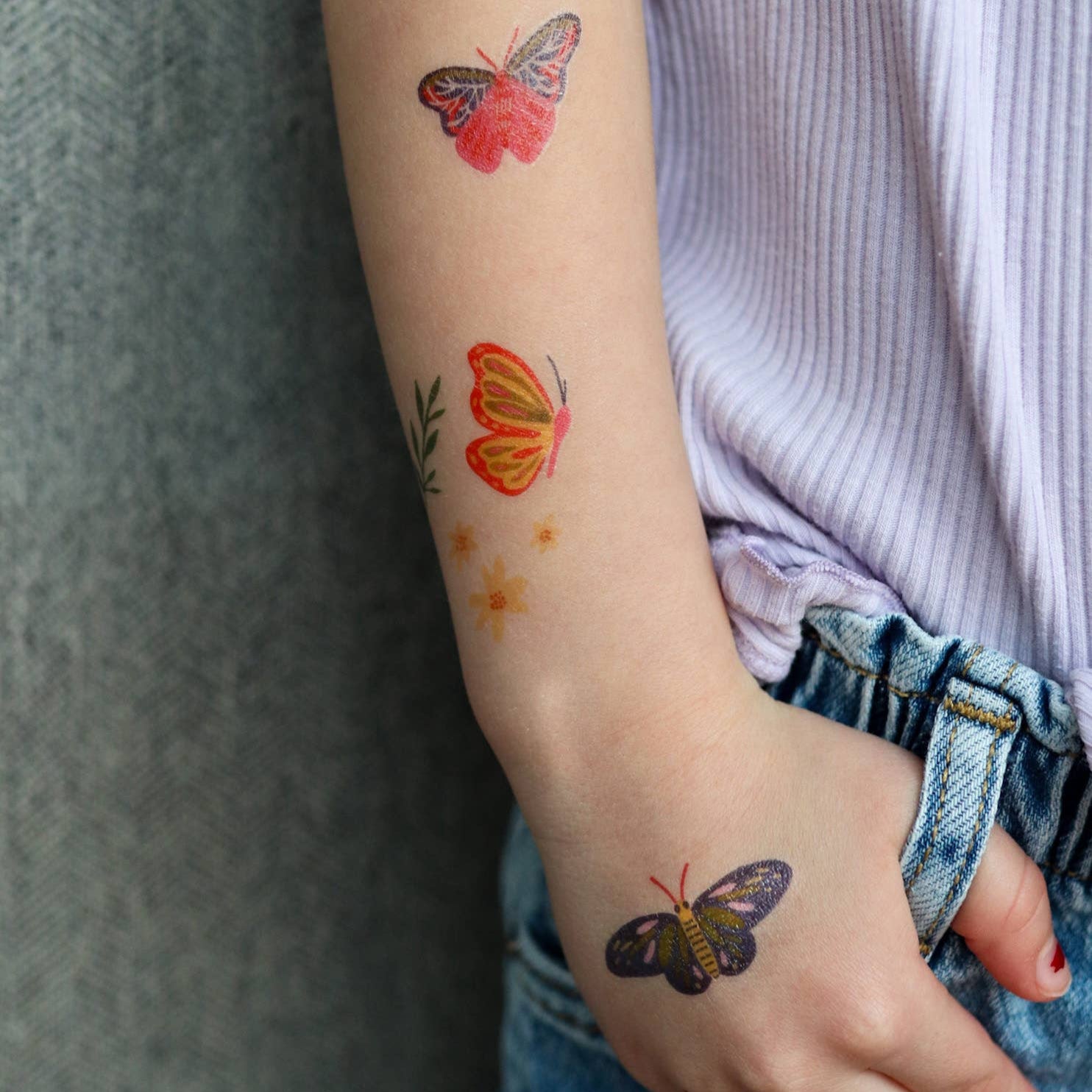 Butterfly tattoos on a person's arm and hand against a neutral background