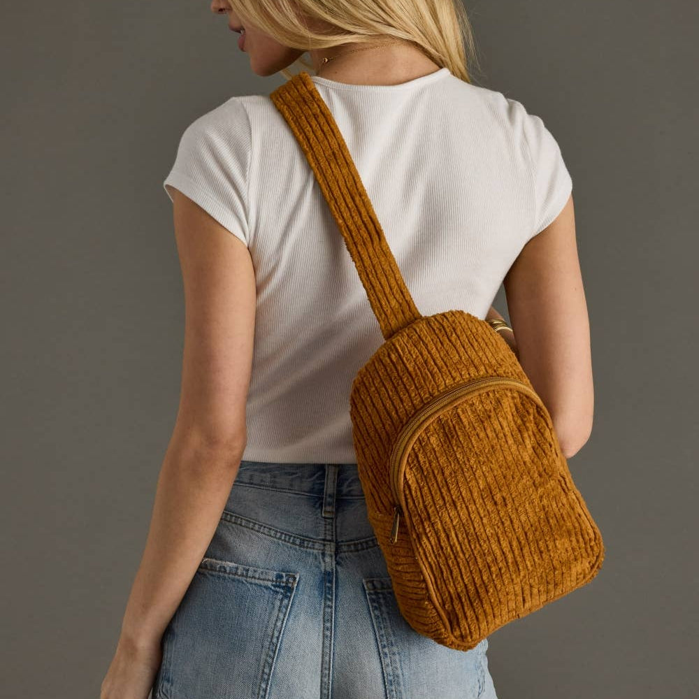 Person wearing a mustard yellow backpack against a gray background