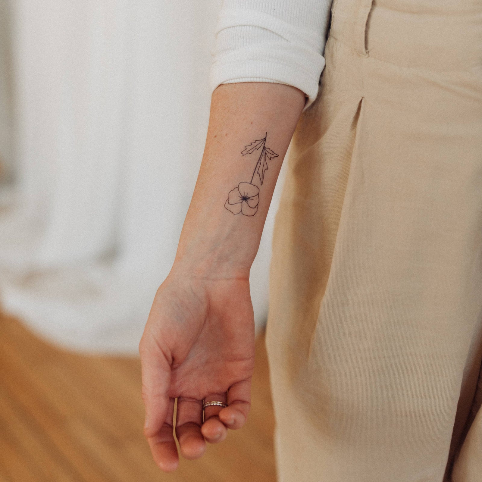 Person wearing beige pants and a white long-sleeve shirt, with a tattoo on their arm.