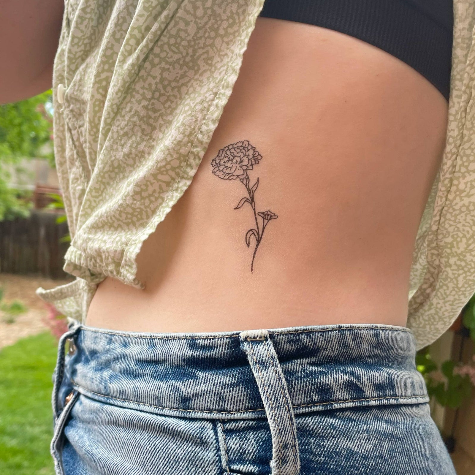 Person wearing blue jeans with a subtle tattoo on the back of their arm, standing outdoors.