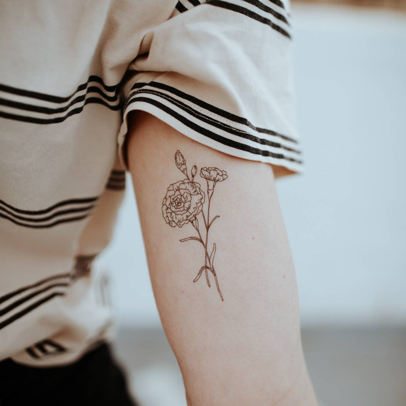 Person wearing a white shirt with black stripes, showing a floral tattoo on their arm.