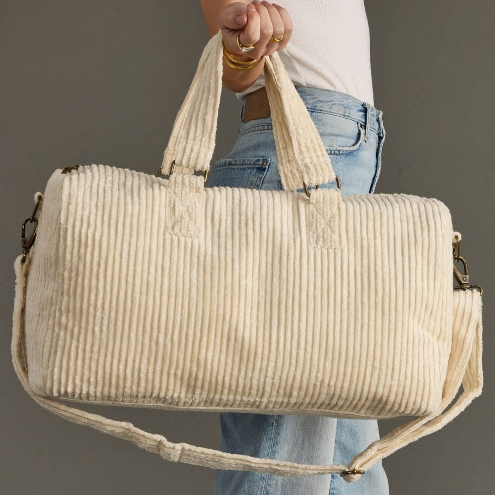 Person holding a beige corduroy duffel bag against a neutral background