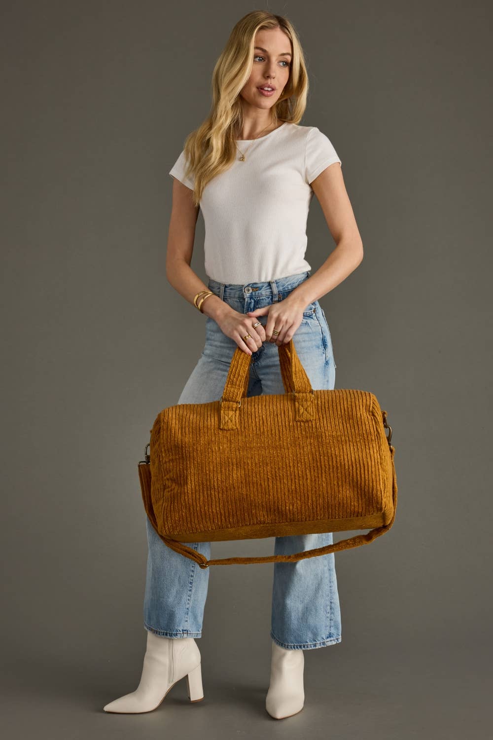 Person holding a mustard yellow corduroy duffel bag against a gray background