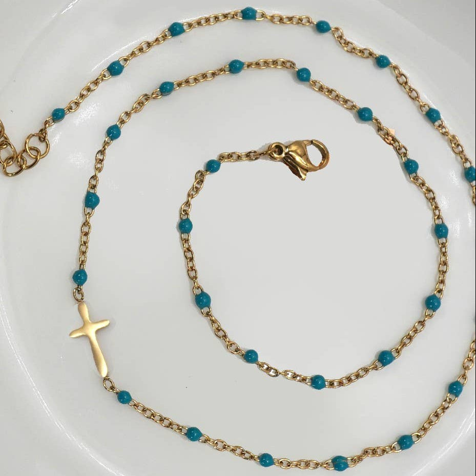 Gold necklace with blue beads on a white plate with a pink background