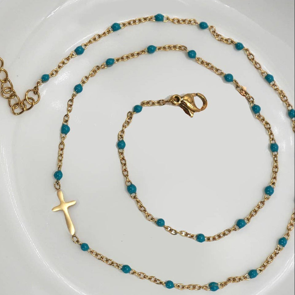 Gold necklace with blue beads on a white plate with a pink background