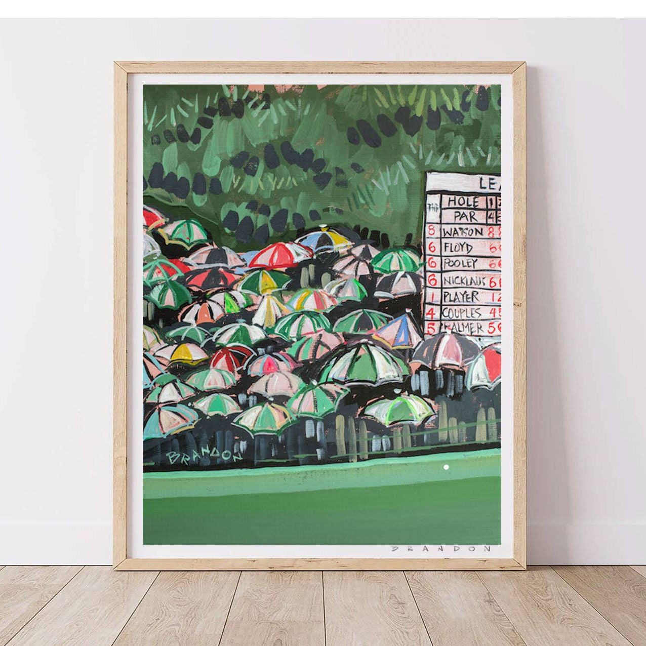 Framed artwork of a colorful scene with umbrellas and a scoreboard on a white wall.