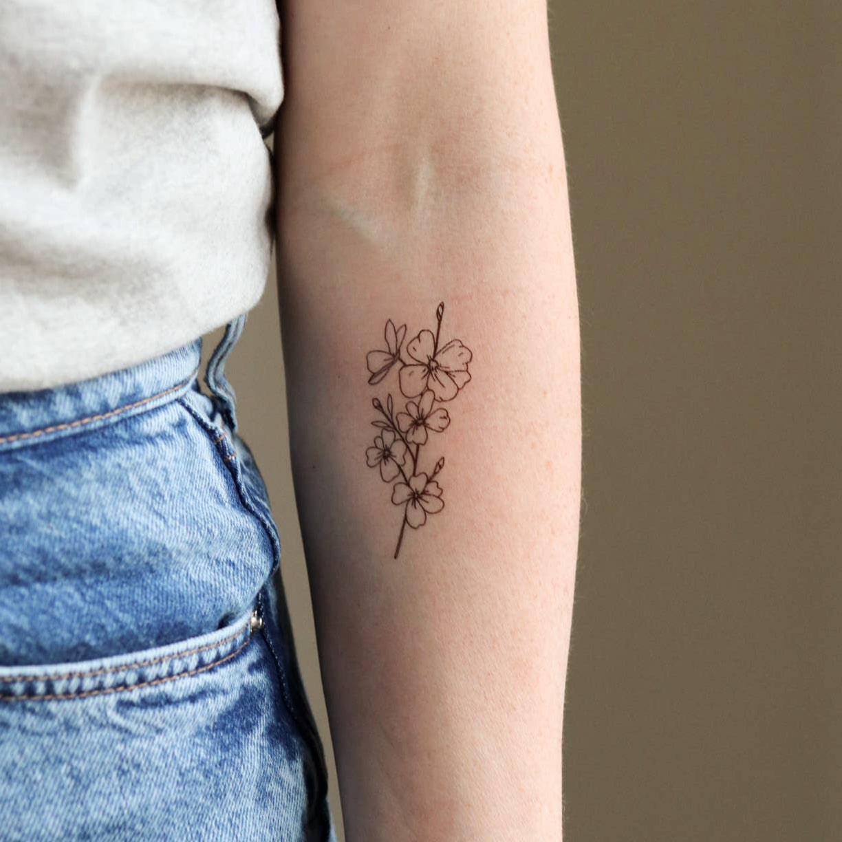 Person wearing a small floral tattoo on their arm against a plain background