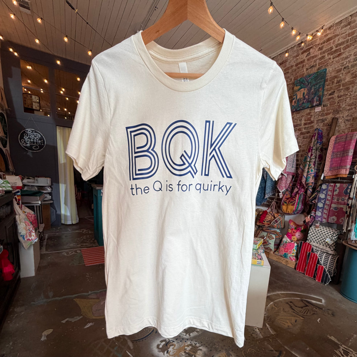Ivory t-shirt with 'BQK the Q is for quirky' text on a hanger in a store.