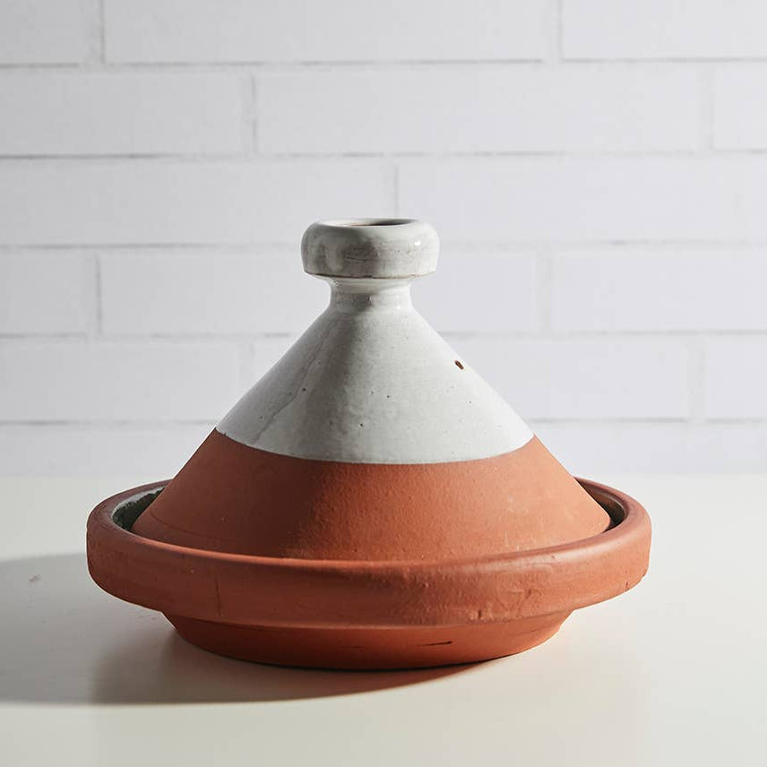 Terracotta tagine with white top on a light surface with a white tiled wall background