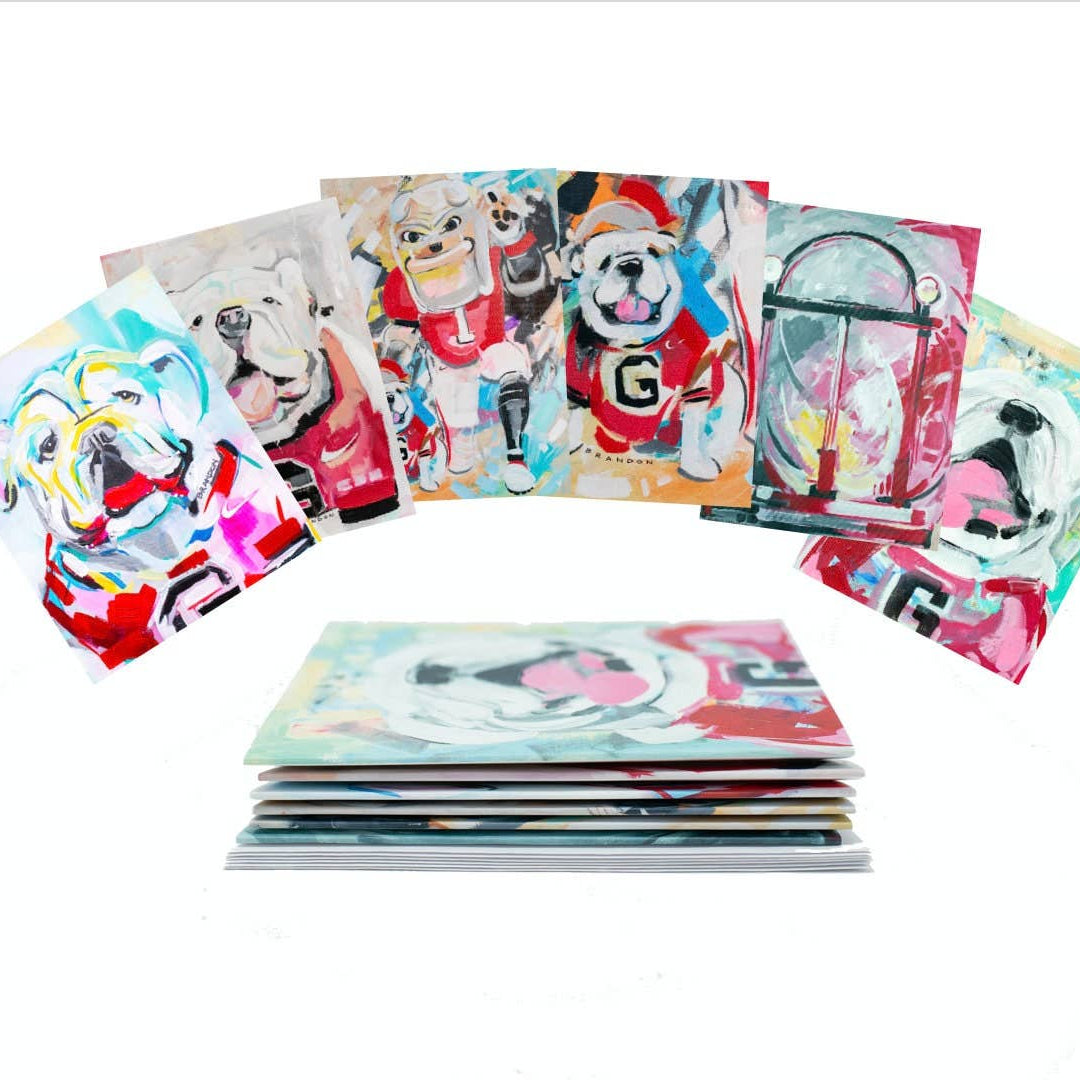 A set of colorful pop-art dog paintings, with several individual prints fanned out above a stack of matching art prints on a white background.