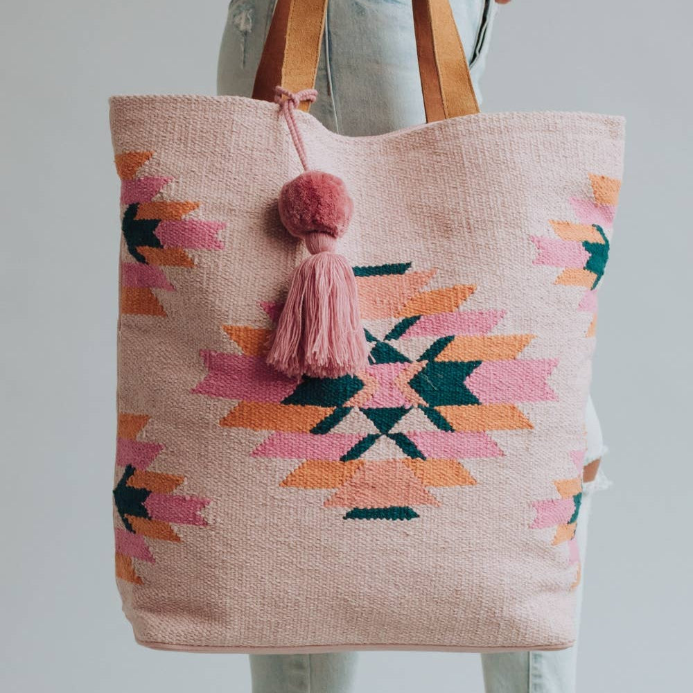 Tote bag with geometric pattern and pink tassel held by a person wearing jeans.