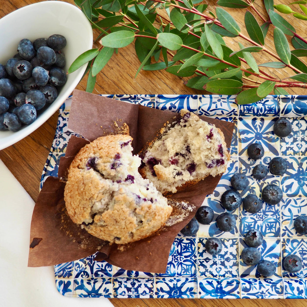 Blueberry muffins on a decorative plate with blueberries and greenery.
