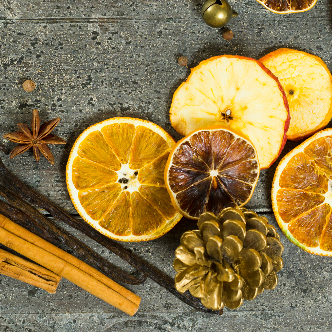 Dried orange slices, cinnamon sticks, and a pine cone on a textured surface