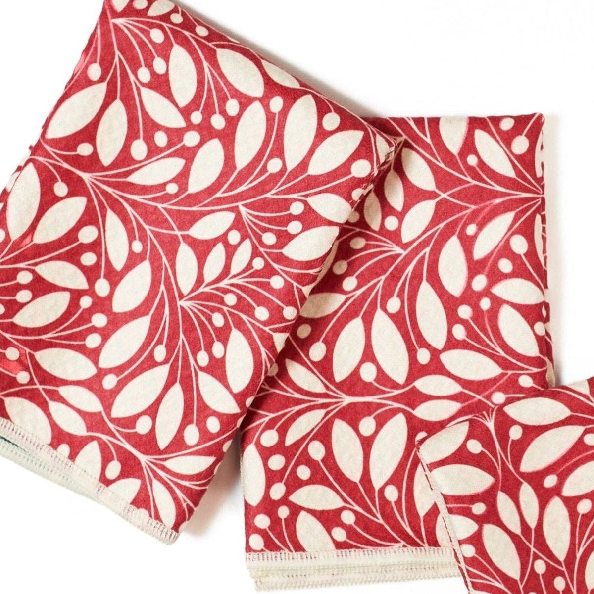 Three folded cotton napkins with a red and cream botanical leaf pattern, arranged on a plain white background.
