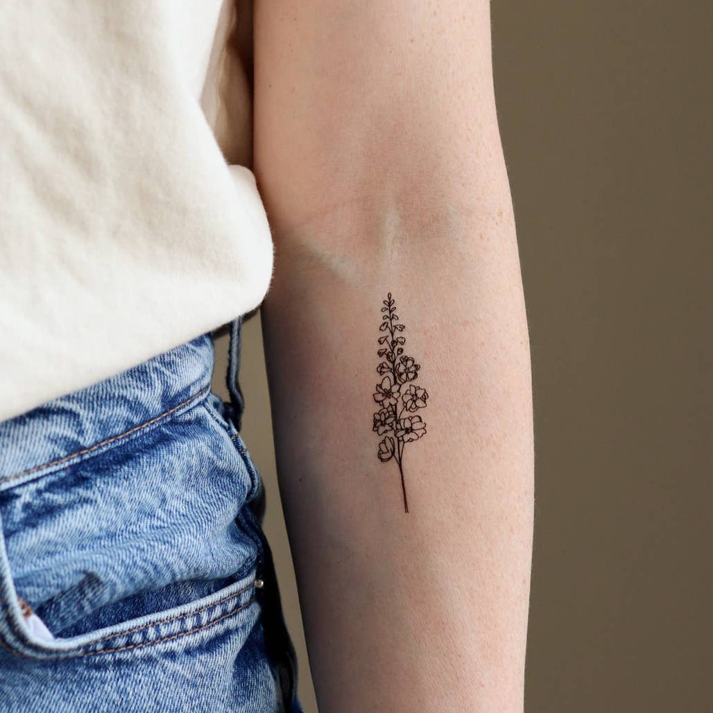 Person wearing a white shirt and blue jeans with a small tattoo on their arm.