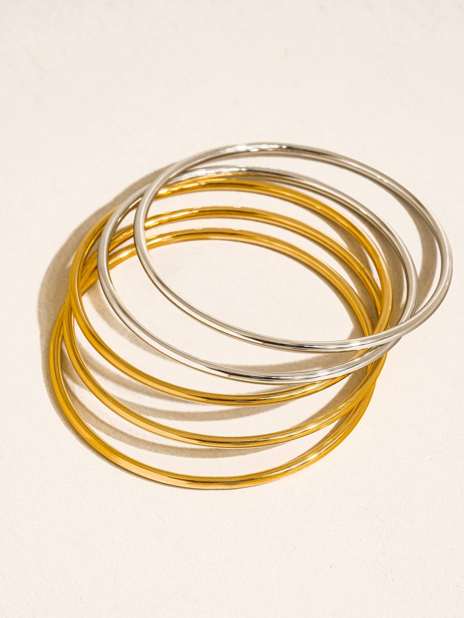 Set of gold and silver bangles on a light beige background