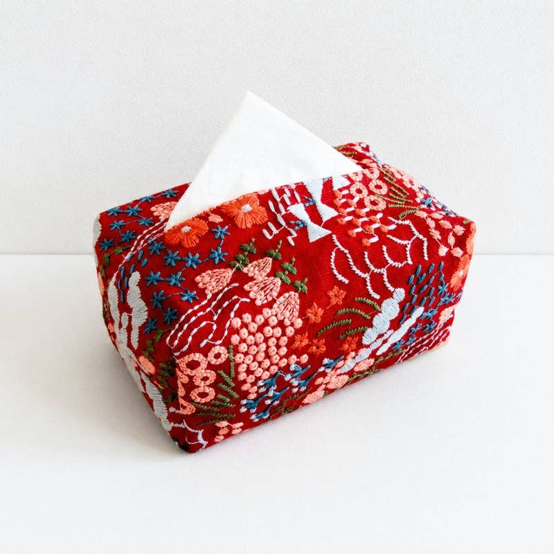 A red embroidered tissue box cover with a white tissue paper partially extended, set against a clean white background.